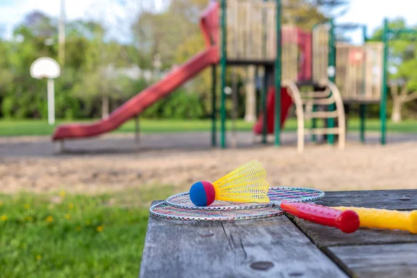 夏の晴れた日に公園の背景にある木製のテーブルと子供たちの遊び場でバドミントンのゲームラケットとシャトルチェック アクティブライフスタイルのコンセプト 家族のための楽しいレジャー活動 — ストック写真