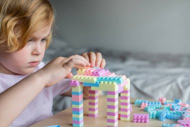 Oyuncak plastik yapı taşlarıyla oynayan, masada oturan güzel bir çocuk. Yaratıcı aktivitelerle meşgul olan küçük bir kız. Çocuklar için iyi motor becerilerinin geliştirilmesi.