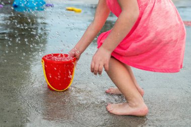 Küçük çocuk sıcak yaz günü yerel halk parkında su ve oyuncaklarla oynuyor. Pembe elbiseli küçük güzel kız çeşme parkında eğleniyor..