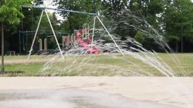 Playground without children in the local public park with working spraying splash pad fountain in summer.