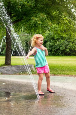 Sıcak bir yaz günü, yerel halk parkında su sıçratma yerindeki suyla oynayan küçük bir çocuk. Küçük güzel kız çeşme bahçesinde eğleniyor..