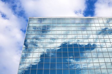 Mavi gökyüzünün yansıması, şehir merkezindeki uzun ve modern cam binada bulutlar.