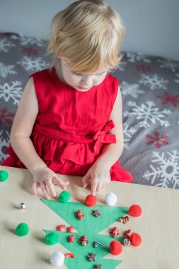 Noel tatili çocukları evde faaliyet gösteriyor. Kırmızı elbiseli küçük bir çocuk küçük ponpon kızlarla Noel ağacı süsleme oyunu oynuyor..