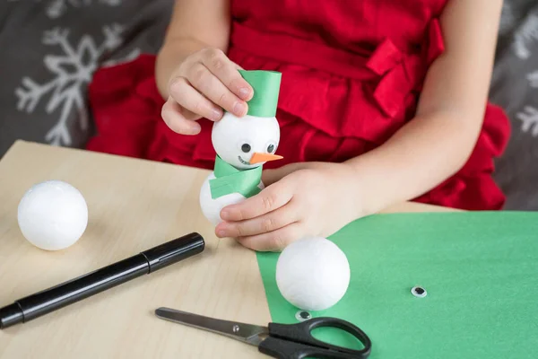 Christmas kids craft activities at home. Little girl making snowman. Kid is busy playing alone.