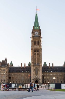 Ottawa, Kanada - 19 Eylül 2021: Kanada 'nın başkentinde Kanada bayrağı taşıyan parlamento binası, Ottawa gökyüzüne karşı. Akşamları 100. yıl alevinin yanında yürüyen insanlar.