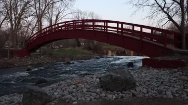 İlkbaharda parkta akarsu üzerinde kırmızı köprü. Kanada, Ontario 'daki Perth kasabasında dere akıyor. İlkbaharda nehir