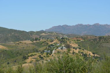 Malibus Verdant Hills 'in nefes kesen manzarasında güneşli bir günde yemyeşil ve tuhaf evlerle dolu sakin bir manzara sergilenir.