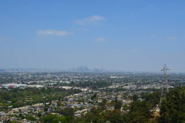 Yüksek bir bakış açısından geniş şehir manzarası aşağılara doğru yayılıyor ve modern binalar ufuk çizgisini deliyor. Bereketli tepeler, parlak mavi bir gökyüzünün altındaki sahneyi çerçeveletip doğal güzellikleri ekliyor..