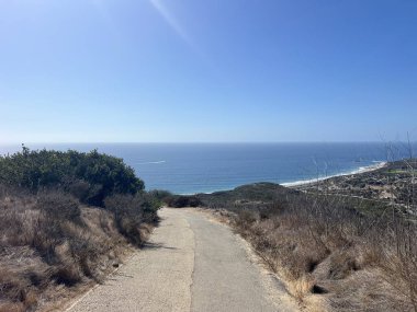 Dolambaçlı bir yol, güneşli ve güneşli bir günde kumlu sahilde hafif dalgalar eşliğinde sakin okyanusu görmenizi sağlar..