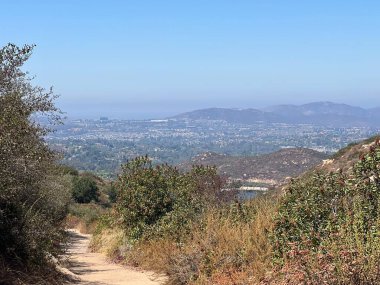 Dolambaçlı toprak yol yemyeşil çalıların arasından geçerek aşağıdaki vadiyi muhteşem bir şekilde gösteriyor. Parlak mavi gökyüzü, sıcak bir öğleden sonra huzurlu manzarayı güzelleştirir..
