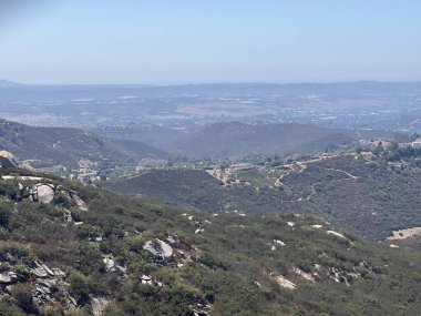 Parlak güneş ışığıyla aydınlatılan dalgalı tepeler ve vadiler boyunca canlı yeşillik yayılır. Uçsuz bucaksız manzara, uzaklara kadar uzanıyor. Huzurlu ve resimsel bir manzara yaratıyor..
