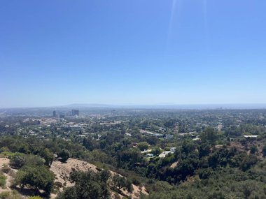 Büyüleyici bir manzara, yemyeşil ve tepelerin arasında yuva yapmış, güneşli bir günde doğa ve kentsel yaşamın karışımını gözler önüne seren geniş bir şehri yakalıyor..