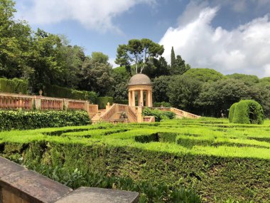 Yeşillik, güzel bir bahçedeki büyüleyici bir çardağı çerçeveler. Ziyaretçiler tertemiz çalıların arasında geziniyor, açık gökyüzünün altında huzurlu bir öğleden sonranın tadını çıkarıyorlar..