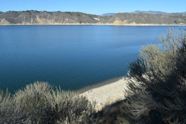 Sakin sular mavi gökyüzünü yansıtırken ziyaretçiler gölde huzurlu bir günün tadını çıkarıyorlar. Manzara, yumuşak tepeleri ve kayalık kıyıları barındırır. Huzuru ve doğanın güzelliğini davet eder..