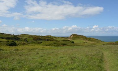Canlı yeşillik tepeleri kaplıyor, ılık meltemde yavaşça sallanıyor. Parlak mavi gökyüzünün altında sakin bir deniz ışıldıyor, huzurlu bir atmosfer yaratıyor sakin bir yürüyüş için mükemmel..