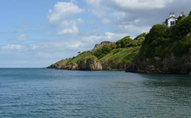 Sakin sahil boyunca uzanan canlı yamaçlar yeşilliklerle kaplanırken, berrak sular mavi gökyüzünü yansıtıyor ve kıyı manzarasında huzurlu bir anı yakalıyor..