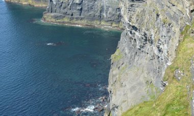 Heybetli uçurumlar kristal gibi berrak bir denizin üzerinde canlı yeşil çimenler kayalıklara tutunuyor. Gökyüzü ışıl ışıl parlıyor, huzurlu manzarayı güzelleştiriyor, huzurlu bir atmosfer yaratıyor..