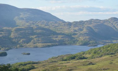 Bereketli yeşil dağlar parlak gölü kucaklıyor, yukarıdaki parlak gökyüzünü yansıtıyor. Uzaktan yükselen tepeler, açık havada keşif için ideal barışçıl bir atmosfer yaratıyor..