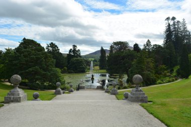 Ziyaretçiler geniş bir yolda yürürler. Çevrelerinde canlı yeşil yapraklar ve zarif taş şekiller vardır. Bu da bizi pitoresk bir gölete ve zarif çeşmelere götürür..