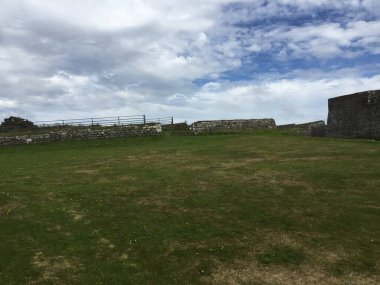 Bulutlar parlak bir gökyüzünde süzülürken, yemyeşil otlar eski taş duvarların etrafına yayılıyor. Huzurlu atmosfer, tarihi keşfetmeye ve yansıtmaya davet ediyor..
