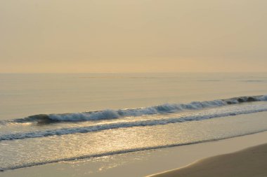 Yumuşak dalgalar, batan güneşin sıcak parıltısını yansıtan kumlu sahile vurur. Huzurlu bir atmosfer bu sakin kıyı bölgesinde yaratılıyor ve rahatlamaya yol açıyor..
