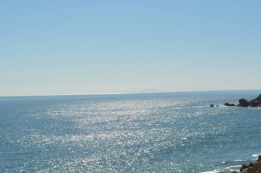 Sakin okyanus ufka doğru uzanırken, parlak dalgalar güneşin sıcak ışınları altında dans ediyor. Kayalık sahilde huzurlu bir an, derin düşüncelere ve rahatlamaya davetiye çıkarır..