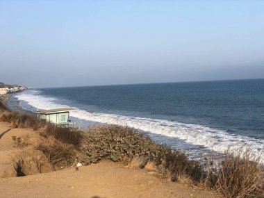 Güneş batmaya başladığında, yumuşak dalgalar kıyıya vurur. Kıyıdaki bitki örtüsüyle çevrili küçük bir sahil kulübesi su kenarında duruyor. Huzurlu sahne rahatlamayı davet eder..