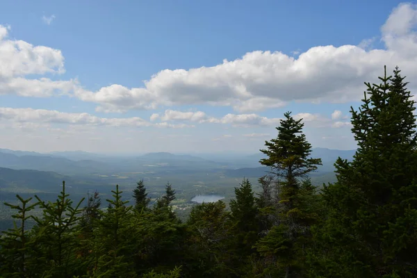 Uçsuz bucaksız yeşil vadiler, parlak mavi bir gökyüzünün altında kabarık bulutlarla kaplı. Çamlar, göller gün ışığında parlarken manzarayı resmediyor ve huzurlu bir geri çekilme yaratıyor..
