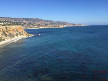 Yumuşak güneş ışığı kayalıkların üzerine sıcak bir parıltı saçarken dalgalar yavaşça kayalık bir kıyı şeridine çarpar. Huzurlu bir atmosfer, doğanın güzelliğinin yansımasını ve tadını davet eder..