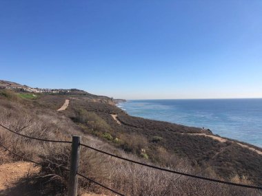 Dönek bir sahil yolu, okyanusun canlı renklerini kahverengi ve yeşil bitki örtüsüne karşı sergiliyor..