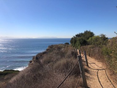 Kuru çalılarla çevrili sarmal bir patika uçurumun kenarına çıkar. Güneş, ufuktaki uzak adaları ortaya çıkararak, okyanusun üzerinde parlak bir şekilde parlıyor..