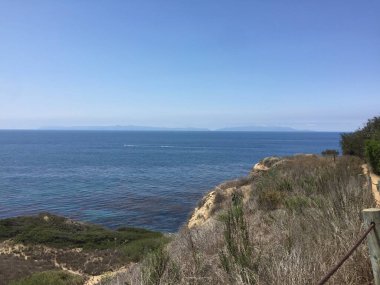 Okyanusun nefes kesici manzarası engebeli kıyı şeridinin ötesine uzanıyor. Sakin su, dalgaların kıyıya hafifçe çarpmasıyla güneşli gökyüzünü yansıtır. Doğa severler için mükemmel bir gün..
