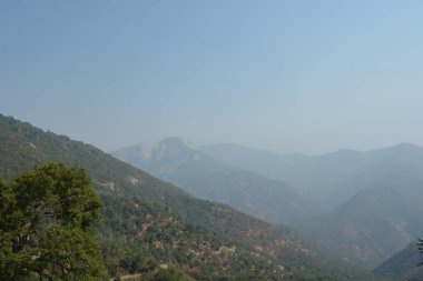 Ufuk boyunca uzanan engin dağlar, yeşil ağaçlarla çevrili. Yumuşak bir sis tepeleri sarıyor ve bu sakin öğleden sonra sakin ama gizemli bir atmosfer yaratıyor..