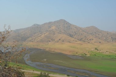 Yuvarlanan tepeler arka planda görkemli bir şekilde yükselirken, sakin bir nehir berrak mavi gökyüzünün altındaki yemyeşil bir vadide dolanıyor. Doğa sükunetle uyanıyor..
