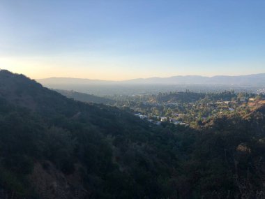 Güneş uzak dağların ardında batarken altın ışık sessiz vadiyi yıkıyor. Aşağıdaki yemyeşil ağaçların ve evlerin üzerine uzun gölgeler bırakıyor. Huzurlu bir sahne yansımayı ve huzuru davet eder..