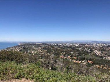 Nefes kesici bir manzara, aşağıdaki yeşil tepelerin çerçevelediği bir kıyı şehrini gözler önüne seriyor. Parlak mavi gökyüzü ve sakin okyanus dinlenmek için mükemmel sakin bir atmosfer yaratır..