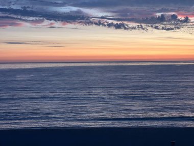 Ufuk, güneş batarken yumuşak renklerle doludur sakin okyanus dalgaları üzerinde dingin bir parıltı bırakır. Hafif dalgalanmalar rengarenk gökyüzünü yansıtıyor. Kumsalda huzurlu bir atmosfer yaratıyor..