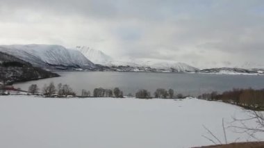 İlkbaharda karla kaplı fiyort boyunca ilerleyen araç