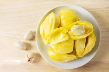 Jackfruit. Taze sarı olgun meyve dilimleri, ahşap masa ve tohumlar üzerinde beyaz tabağa yerleştirilmiş lezzetli tatlılar. Egzotik tropikal vejetaryen meyvesi.