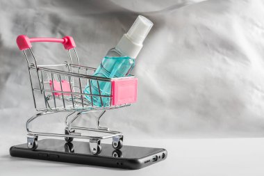 Siyah akıllı telefon ve beyaz fon üzerinde alışveriş arabasında alkol spreyi. Evden ve teslimattan online alışveriş. Alkol el yıkama spreyi. Koronavirüs önleyici Sars-nCoV-2, antibakteriyel el dezenfektanlı Covid-19 enfeksiyonu.