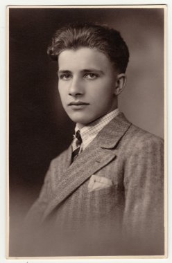 Bir vintage studio fotoğraf gösterileri genç adam giyer lüks ceket. Antik siyah ve beyaz fotoğraf.