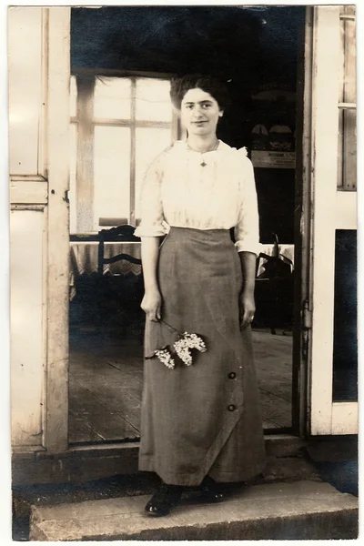 Foto vintage mostra mulher fica na frente da casa e detém um lilás. Retrato de estúdio preto e branco . — Fotografia de Stock