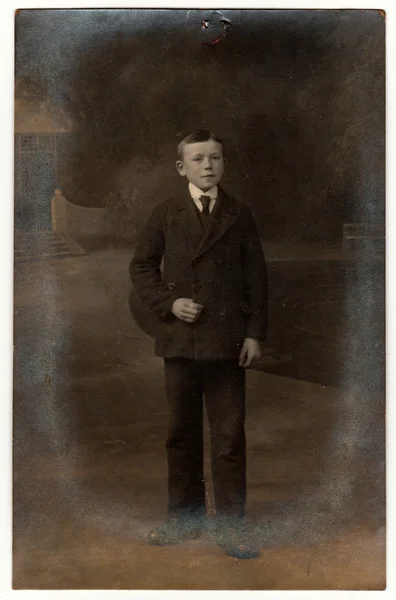 复古照片显示男孩穿西装打领带。在户外拍摄的古董黑白照片。图像顶部是绘图销的印记。照片有深色色调. — 图库照片