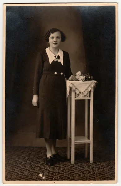 Vintage photo shows woman wears an elegant dress, poses next to white table. Black & white antique studio photography with sepia effect. — Stock Photo, Image
