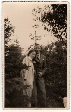 Vintage photo shows woman and man pose in the forrest. Black & white antique photography.