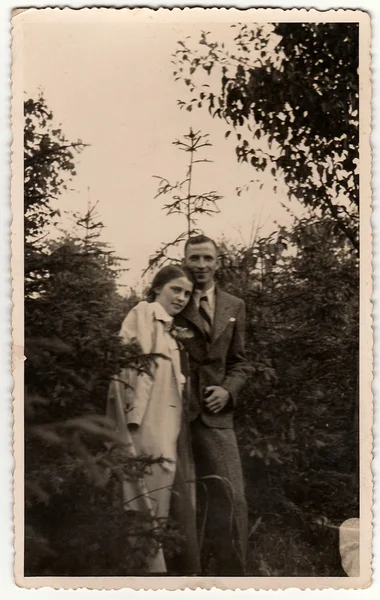 Vintage photo shows woman and man pose in the forrest. Black & white antique photography.