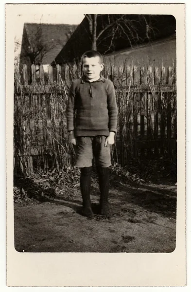 Vintage photo shows young boy (pupil, student) stands in front of wooden fence. Black & white antique photography. — Stock Photo, Image