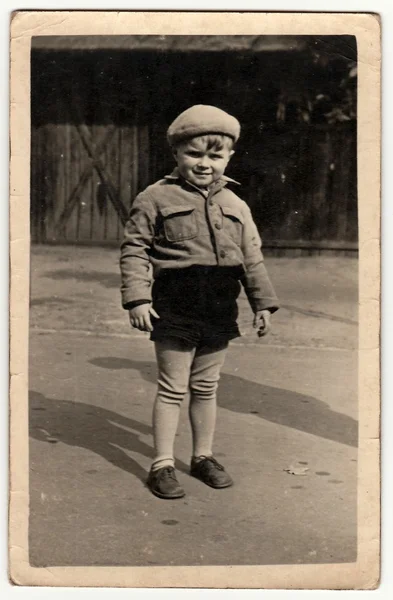 Ein altes Foto zeigt einen kleinen Jungen, der im Hinterhof posiert. Schwarz / weiß antikes Foto. — Stockfoto