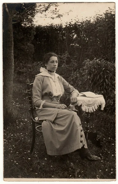 Photo vintage montre femme assise sur une chaise historique à la petite table dans le jardin. Photographie antique noir & blanc . — Photo