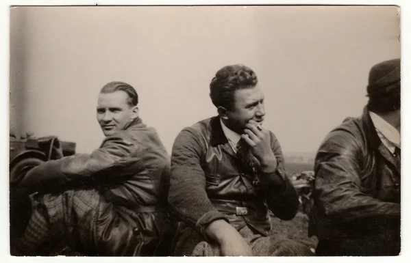 Vintage photo shows men wear leather jacket and vest. They have a rest after car trip. Black & white antique photography. — Stock Photo, Image